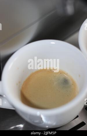 Espresso appena fatto in tazza piccola su fondo metallico. Preparazione del caffè mattutino a casa. Foto Stock