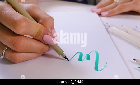 Le mani del calligrafo scrivono la parola su carta bianca. Iscrizione di lettere ornamentali decorate. Calligraphy, graphic design, lettering, graphic writing, creation Foto Stock