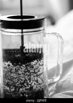 Una foto verticale in scala di grigi di un French Press con tè alle erbe Foto Stock