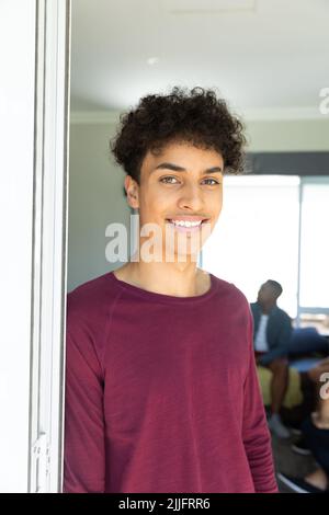 Ritratto di un bel giovane caucasico sorridente con capelli ricci in piedi dalla finestra di casa Foto Stock