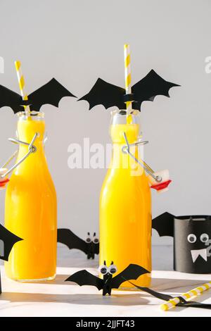 Halloween mocktail. Cocktail analcolico all'arancia per la festa di Halloween su un tavolo bianco. Le cannucce sono decorate con pipistrelli di carta tagliati. Halloweens spooky Foto Stock