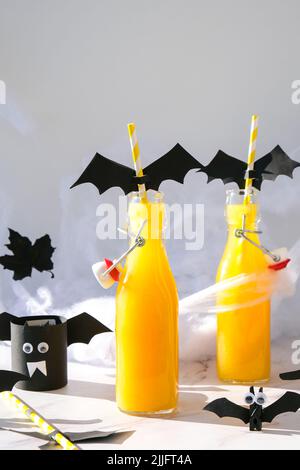 Halloween mocktail. Cocktail analcolico all'arancia per la festa di Halloween su un tavolo bianco. Le cannucce sono decorate con pipistrelli di carta tagliati. Halloweens spooky Foto Stock