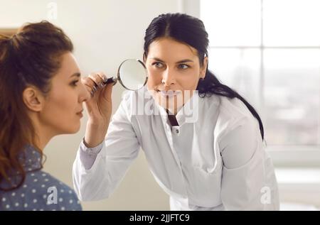 Dermatologo con lente d'ingrandimento guarda il talpa o la pigmentazione sul volto della donna Foto Stock