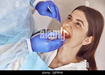 Il medico professionale sta facendo la chirurgia dentaria per felice donna caucasica nel gabinetto dentale moderno Foto Stock