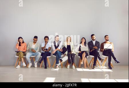 Gruppo di persone multirazziali stanno aspettando il loro turno per l'intervista seduta su sedie in fila. Foto Stock