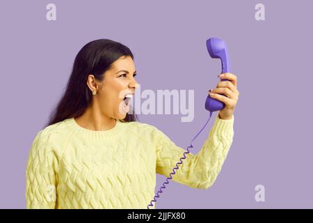 Giovane donna che tiene il telefono fisso e urla nervosamente per le chiamate con fastidioso pubblicità Foto Stock