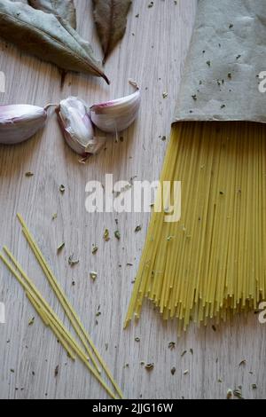 Fascio di spaghetti italiani legati con aglio, cipolla, origano e foglie di alloro su sfondo ligneo Foto Stock