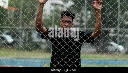 Sconvolto l'uomo africano appoggiato su una recinzione metallica. Arrabbiato persona nera scuotendo recinzione Foto Stock