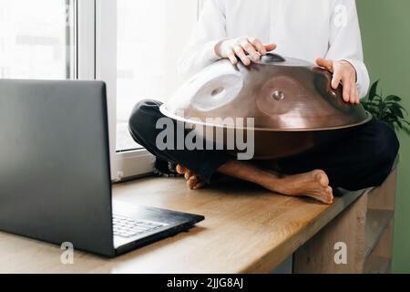 Uomo che suona su un tamburo appeso, o acciaio tamburo, Hangpan, moderno strumento di musica in acciaio a casa. Musica di meditazione per il relax. Impara a insegnare i corsi on-line su Foto Stock