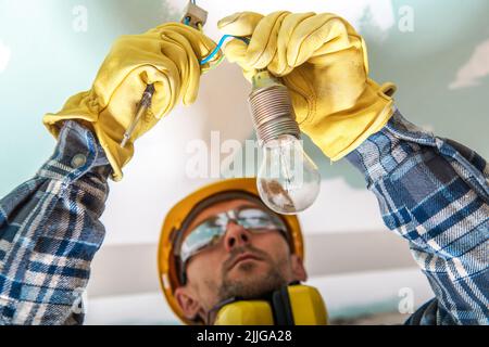 Primo piano di un elettricista professionista specializzato che verifica la corretta installazione dei cavi per l'illuminazione in un'unità residenziale di nuova costruzione. Foto Stock