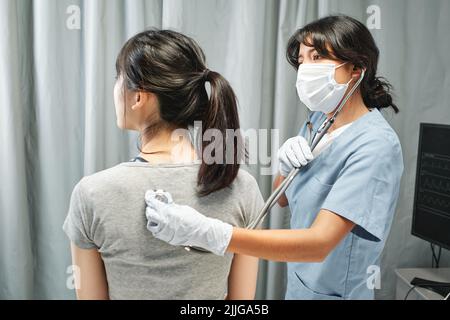 Medico moderno che utilizza stetoscopio ascoltare il suono del cuore e dei polmoni del giovane paziente in pronto soccorso Foto Stock