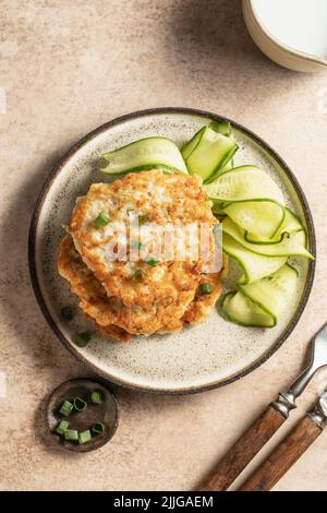 Frittelle di zucchine vegetariane con cipolla verde, cetrioli e salsa cremosa su sfondo marrone con posate. Vista dall'alto. Disposizione piatta Foto Stock