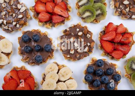 sfondo di appetitose cialde dolci con cioccolato spalmato, noci e frutta su sfondo bianco. Estate, sfondo luminoso e alla moda, design alimentare. Foto Stock