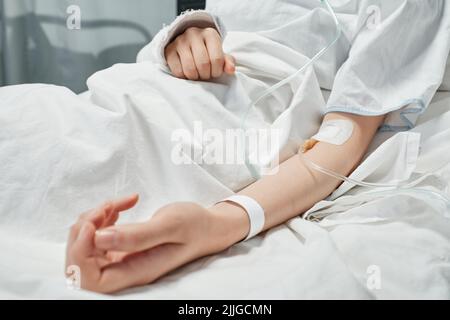 Shot orizzontale di paziente femminile non riconoscibile che riceve farmaci o fluidi nutrienti attraverso la linea endovenosa Foto Stock
