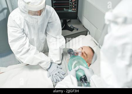 Inquadratura ad angolo elevato di lavoratori medici non riconoscibili che indossano dispositivi di protezione personale che eseguono la RCP per l'uomo maturo Foto Stock