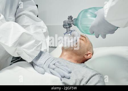 Lavoratori medici professionisti non riconoscibili che indossano dispositivi di protezione personale che eseguono la RCP per l'uomo maturo Foto Stock