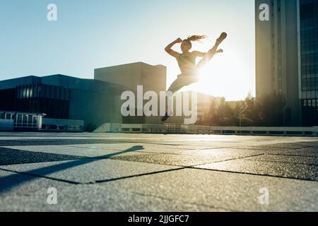 Giovane atleta femminile che pratica le arti marziali a mezz'aria calcia in città. Donna che fa tondo casa all'aperto. Foto Stock