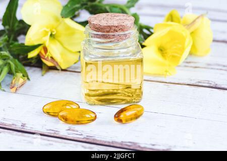 Sera olio di primrose in bottiglia, pillole e fiori su tavola di legno, essenza di biennis Oenotha Foto Stock