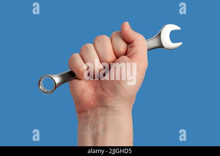 La mano dell'uomo tiene una chiave isolata su sfondo blu. Primo piano. Maschio a mano con chiave cromata. Concetto di assistenza o riparazione Foto Stock