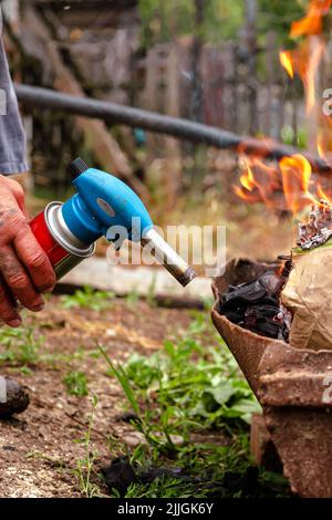 Accensione con bruciatore. Un uomo mette il fuoco a legna con un bruciatore a gas. Allevamento di un fuoco. Abilità di viaggio. Cucinare su un fuoco nella foresta. Foto Stock