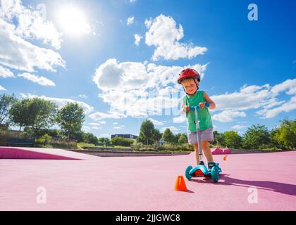 Ragazzo sul calcio scooter giro intorno ai coni arancioni al parco skate Foto Stock