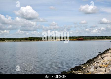 Il 13 maggio 2018 una locomotiva diesel di classe 66 trasporta un treno di vagoni di zavorra vuoti attraverso la baia di Hole, Poole. Foto Stock