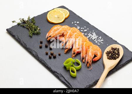 Gamberetti, limone, allspice in cucchiaio e rametto di timo su tavola di pietra. Vista dall'alto. Sfondo bianco Foto Stock