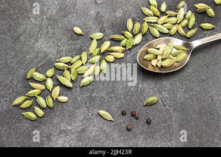 Semi di cardamomo in cucchiaio di metallo e sparsi sul tavolo. Spazio di copia. Disposizione piatta. Sfondo nero Foto Stock