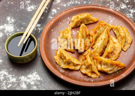 Chopsticks su ciotola con salsa di soia. Gnocchi Gyoza su piastra di ceramica su vassoio arrugginito cosparso di farina. Vista dall'alto Foto Stock