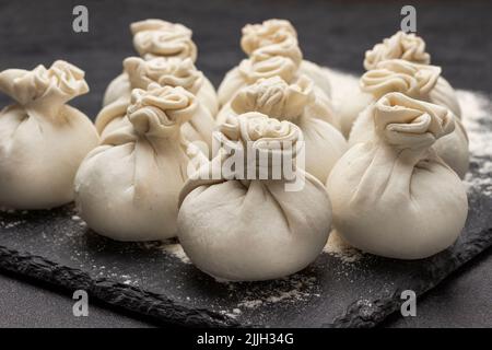 Gnocchi khinkali crudi su tavola di pietra. Primo piano. Sfondo nero Foto Stock