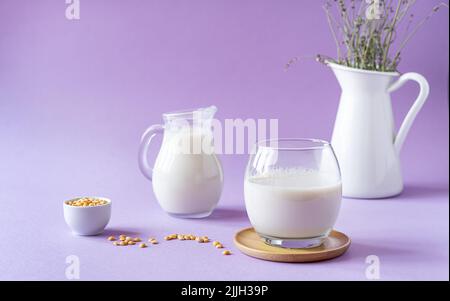 Latte di pisello sano vegano in vetro e vasetto, semi di piselli e caraffa bianca con lavanda. Sfondo lilla. Spazio di copia Foto Stock