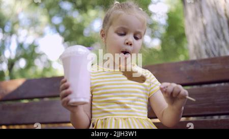 Odessa, Ucraina, Europa dell'Est. 26th luglio 2022. La ragazza della tartaruga mangia un pan di zenzero colorato e tiene un milkshake in mano. Primo piano di ragazza carina bambino seduto sul panchina del parco e mangiare biscotti con un milkshake. (Credit Image: © Andrey Nekrasov/ZUMA Press Wire) Foto Stock