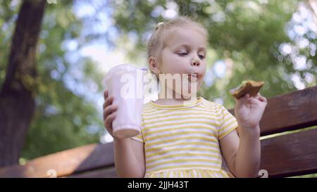 Odessa, Ucraina, Europa dell'Est. 26th luglio 2022. La ragazza della tartaruga mangia un pan di zenzero colorato e tiene un milkshake in mano. Primo piano di ragazza carina bambino seduto sul panchina del parco e mangiare biscotti con un milkshake. (Credit Image: © Andrey Nekrasov/ZUMA Press Wire) Foto Stock