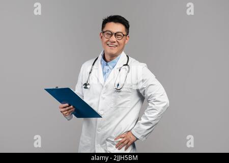 Ritratto di buon sicuro medico asiatico adulto in cappotto bianco, occhiali con stetoscopio e tablet guardare la fotocamera Foto Stock