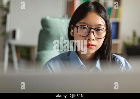 Giapponese Business Female indossando gli auricolari utilizzando il computer al Workplace Indoor Foto Stock