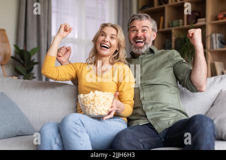 Tempo libero nazionale. I coniugi di mezza età eccitati guardano lo sport in TV a casa Foto Stock