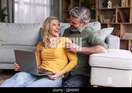 Uomo e donna di mezza età che si divertano con il notebook a casa Foto Stock