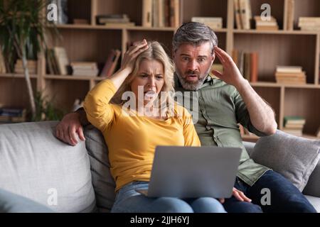 Truffa online. Coppia emozionale di mezza età che guarda lo schermo del notebook con la scarica Foto Stock