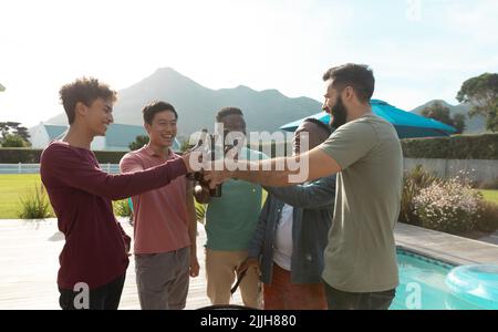Amici maschili multirazziali che brinda bottiglie di birra mentre si diverte al barbecue nel cortile Foto Stock