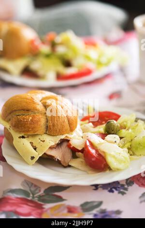 Panino fresco con prosciutto e formaggio e insalata estiva con lattuga, pomodori, formaggio feta Foto Stock