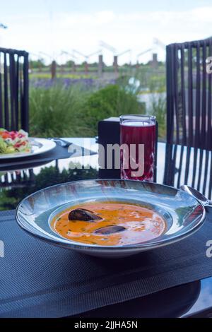 Deliziosa zuppa di pesce di pomodoro bouillabaisse con gamberi, cozze e pesce in un piatto blu sul tavolo. Deliziosa cena romantica a base di pesce Foto Stock