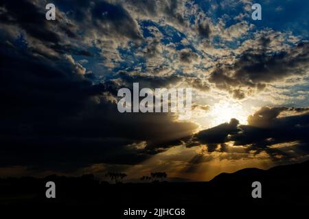 Tramontare il sole splende attraverso nuvole sparse, lasciando belle ombre e colori come blu, giallo, nero, arancione e bianco. Rovina africana tramonti Foto Stock