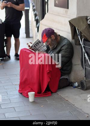 Londra, Regno Unito - 11 settembre 2021: Un uomo senza tetto che legge un libro, seduto su un marciapiede Foto Stock