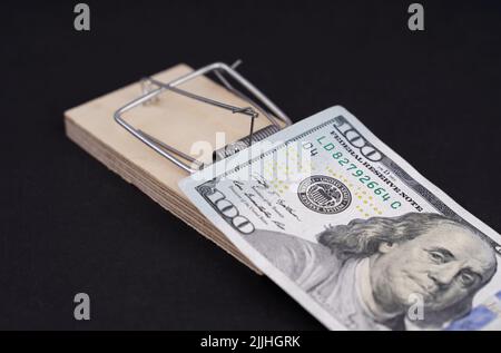 Un conto di cento dollari in un mousetrap di legno su uno sfondo nero. Il concetto di rischi e di investimenti pericolosi. Foto Stock