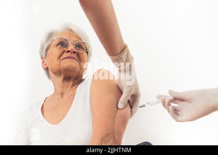 Una vecchia donna felicissima dai capelli grigi che riceve un vaccino per proteggersi dal virus. Foto di alta qualità Foto Stock