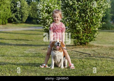 piccola ragazza bianca sta giocando con un cane beagle. foto sparare in estate sulla strada Foto Stock