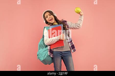il bambino scioccato ascolta la musica in cuffie portare zaino con libro degli esercizi e mela, pranzo. Foto Stock