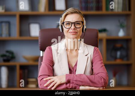 Ritratto di una donna d'affari sorridente che indossa una cuffia in ufficio. Operatore telefonico del supporto clienti soddisfatto presso il call center. Videoconferenza online Foto Stock