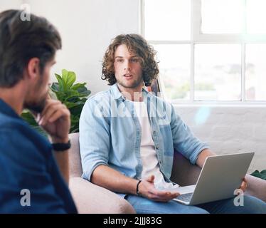 giovane uomo che uisng laptop chattando ad amici brainstorming idee per il progetto seduto sul divano a casa Foto Stock