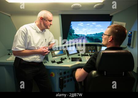 PRODUZIONE - 30 giugno 2022, Saarland, Saarbrücken: Ulrich Pietsch, responsabile DB Training (l), parla con Andreas Lutz, seduto al posto di guida del simulatore ferroviario di Saarbrücken. Tutti i macchinisti devono far testare ogni anno le proprie abilità di guida nel simulatore. (A dpa: 'Basta lasciare che rotoli - come i macchinisti del treno imparano a risparmiare energia') Foto: Oliver Dietze/dpa Foto Stock